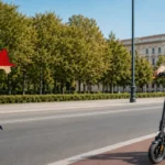 Muškarac s kacigom vozi električni romobil biciklističkom stazom u gradu.