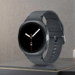 Samsung Galaxy Watch 8 sa tamnosivom narukvicom postavljen na moderno mat postolje ispred minimalističkog betonskog zida